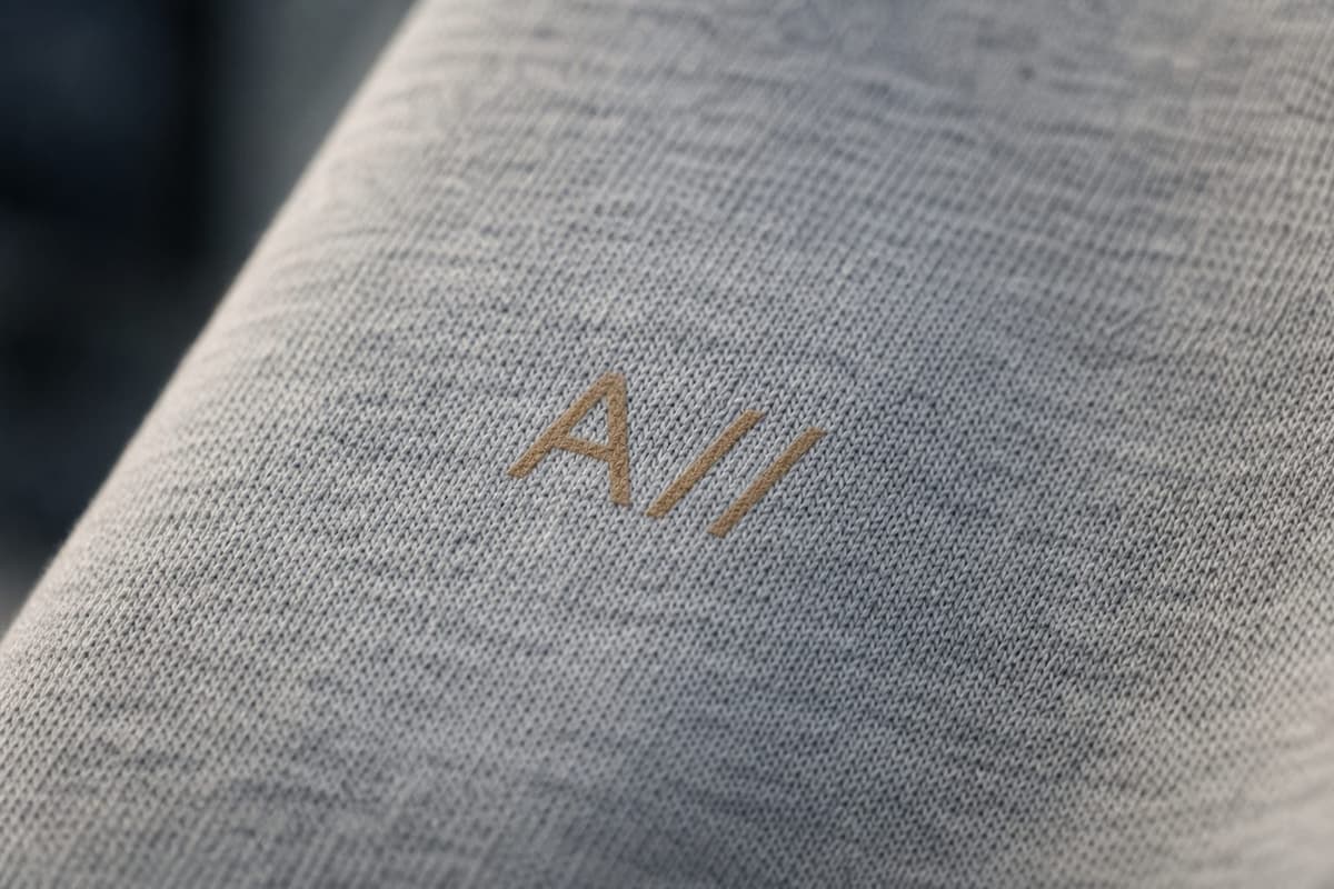 A close-up of the brass A// monogram on heather-gray fabric
